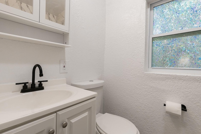 half bath with a textured wall, vanity, and toilet