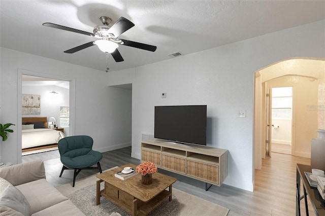 living area with arched walkways, ceiling fan, visible vents, baseboards, and light wood-style floors