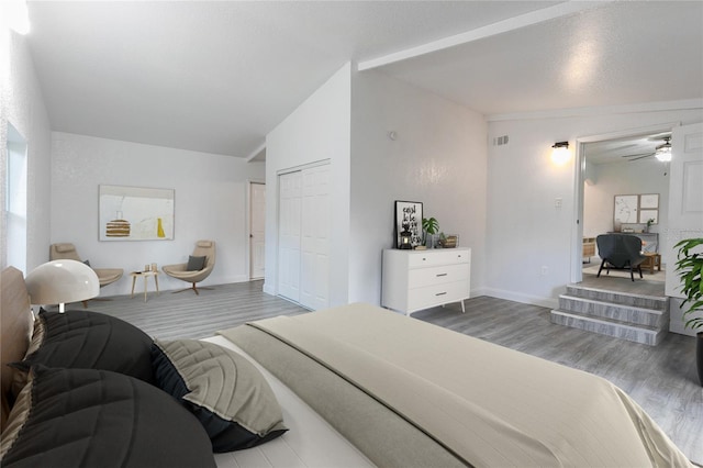 bedroom featuring a closet, visible vents, vaulted ceiling, wood finished floors, and baseboards