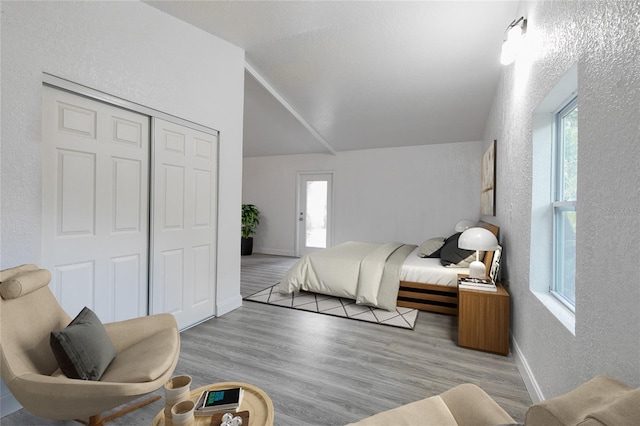 bedroom with lofted ceiling, multiple windows, a textured wall, and wood finished floors