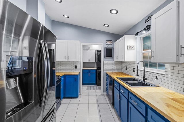 kitchen featuring black appliances, blue cabinetry, butcher block countertops, white cabinetry, and stacked washer / drying machine