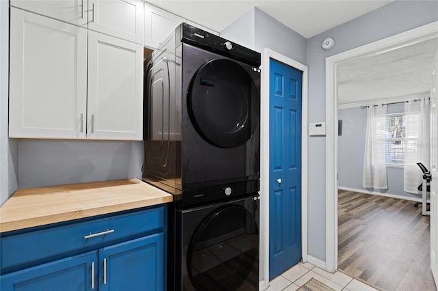 laundry room with cabinets, stacked washer and dryer, and light hardwood / wood-style floors