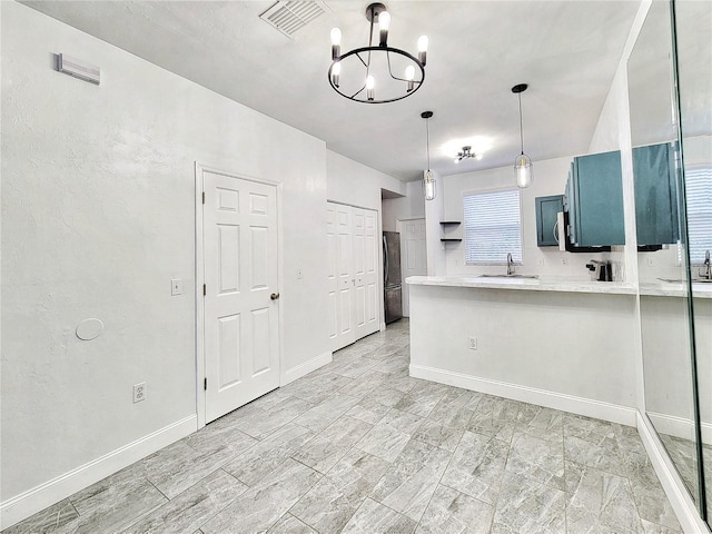 kitchen featuring refrigerator, blue cabinets, sink, kitchen peninsula, and a chandelier