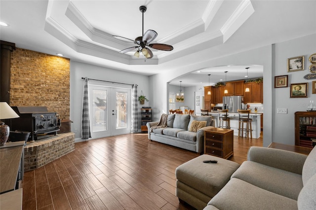 living room featuring ceiling fan, a wood stove, ornamental molding, and a tray ceiling