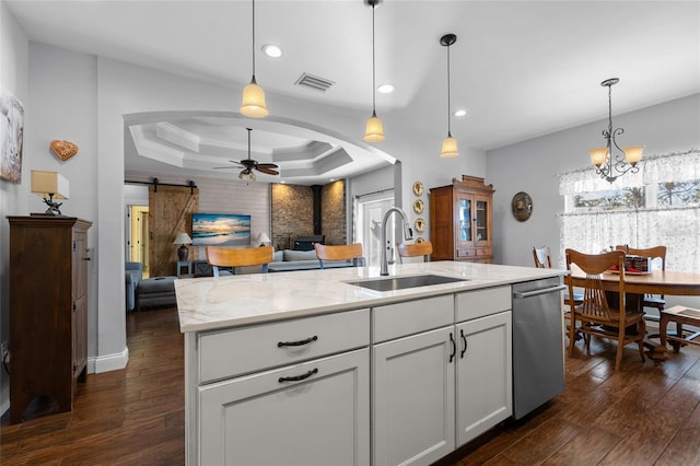 kitchen featuring a center island with sink, sink, a barn door, a tray ceiling, and white cabinetry