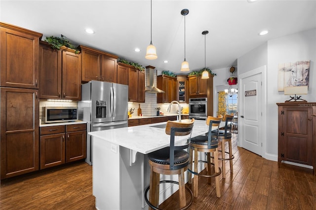 kitchen with a kitchen breakfast bar, wall chimney exhaust hood, stainless steel appliances, decorative light fixtures, and a center island with sink