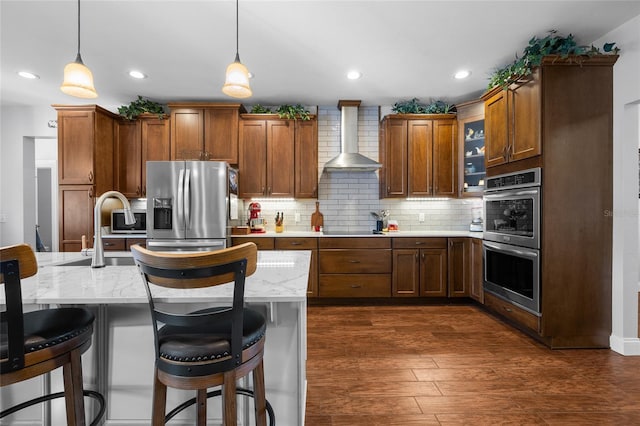 kitchen featuring pendant lighting, wall chimney exhaust hood, appliances with stainless steel finishes, tasteful backsplash, and a breakfast bar area