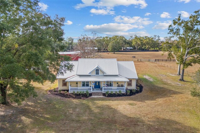 view of front of house with a rural view, covered porch, and a front yard