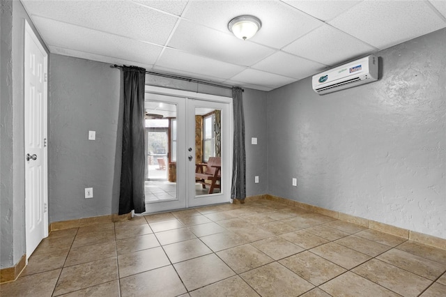 empty room with a drop ceiling, light tile patterned flooring, a wall mounted AC, and french doors