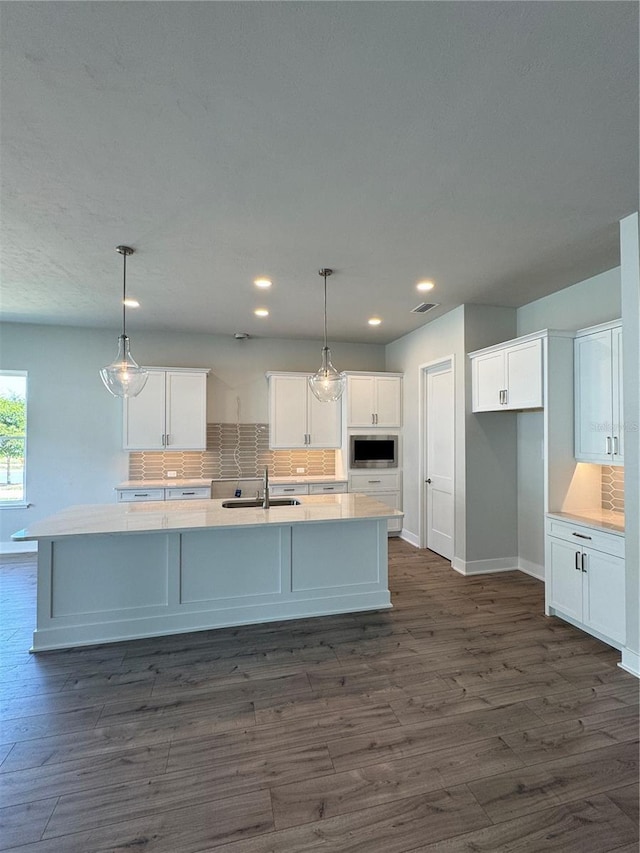 804 SW 144th Dr, Newberry, FL 32669 - kitchen with backsplash, a center island with sink, white cabinetry, dark wood finished floors, and stainless steel microwave