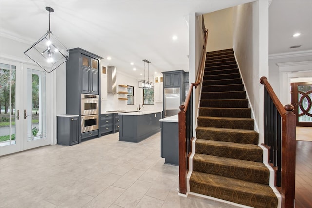 kitchen with ornamental molding, stainless steel appliances, wall chimney range hood, decorative light fixtures, and a kitchen island