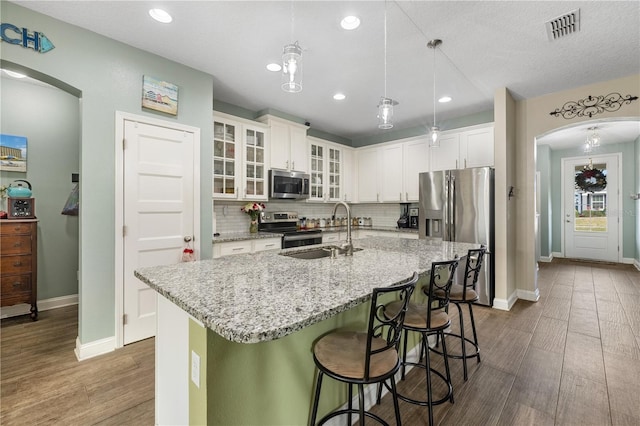 kitchen with appliances with stainless steel finishes, light wood-type flooring, sink, white cabinetry, and an island with sink