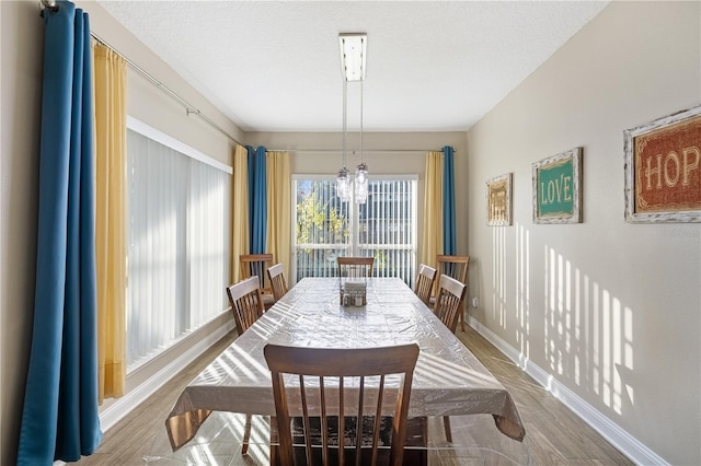 dining area with wood-type flooring, a textured ceiling, and an inviting chandelier