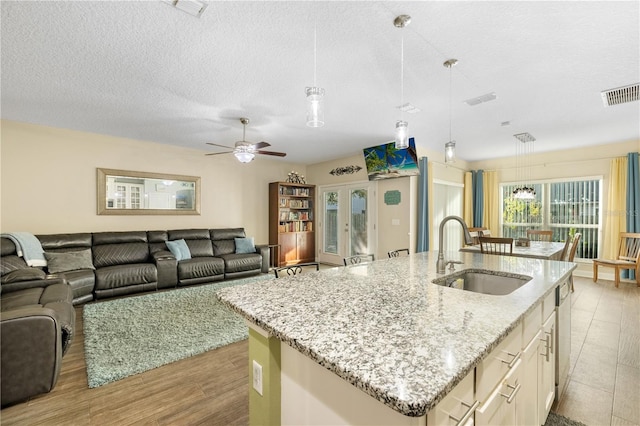 kitchen with decorative light fixtures, light hardwood / wood-style floors, a center island with sink, and sink