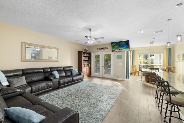 living room with french doors, a healthy amount of sunlight, a textured ceiling, and light hardwood / wood-style flooring