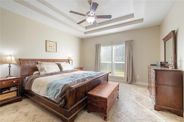 bedroom with a textured ceiling, ceiling fan, light carpet, and a tray ceiling