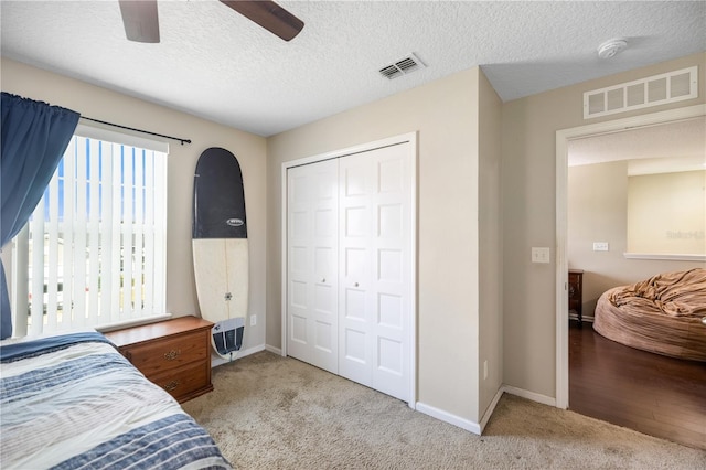 bedroom with a textured ceiling, a closet, ceiling fan, and light colored carpet