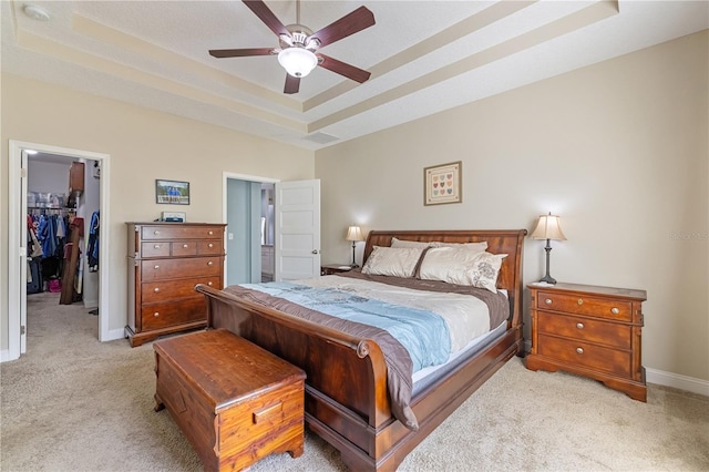 bedroom featuring a walk in closet, a tray ceiling, light colored carpet, ceiling fan, and a closet