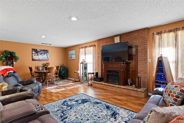 living room featuring hardwood / wood-style flooring, a brick fireplace, and a textured ceiling