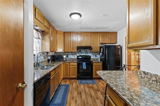 kitchen featuring stone counters, sink, light wood-type flooring, and black appliances