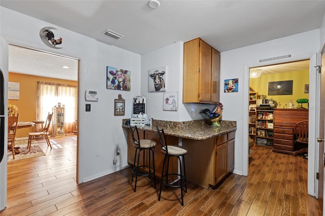 kitchen with a breakfast bar area, dark stone counters, dark hardwood / wood-style flooring, and kitchen peninsula