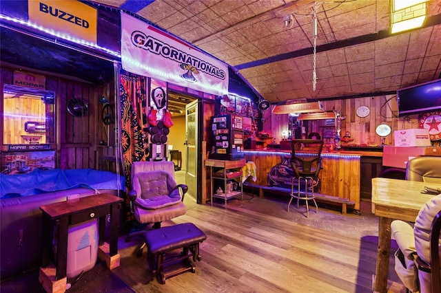 recreation room with hardwood / wood-style flooring, vaulted ceiling, bar, and wood walls