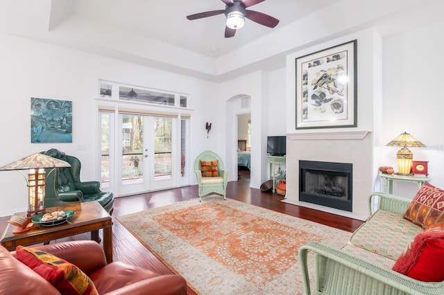 living room featuring french doors, a raised ceiling, dark hardwood / wood-style floors, ceiling fan, and a tiled fireplace