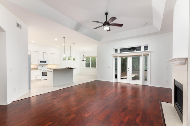 unfurnished living room with light wood-style flooring, a fireplace, a raised ceiling, and visible vents