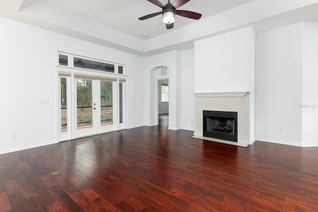 unfurnished living room featuring baseboards, arched walkways, a raised ceiling, and wood finished floors