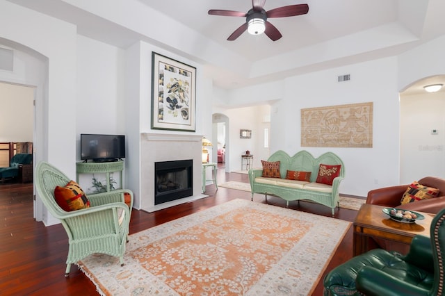 living room with dark wood-style floors, arched walkways, a tray ceiling, visible vents, and a fireplace with flush hearth