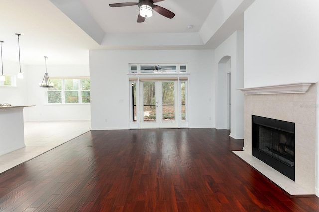 unfurnished living room featuring a tray ceiling, a fireplace, ceiling fan, wood finished floors, and baseboards