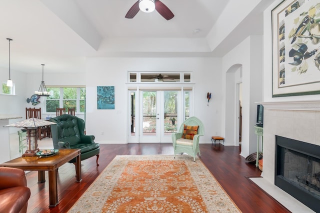 living area featuring a tray ceiling, a tiled fireplace, arched walkways, and dark wood-type flooring