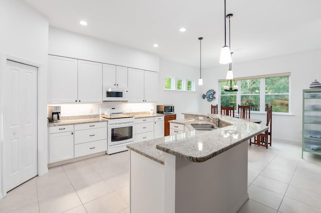 kitchen with white appliances, white cabinets, a sink, and an island with sink