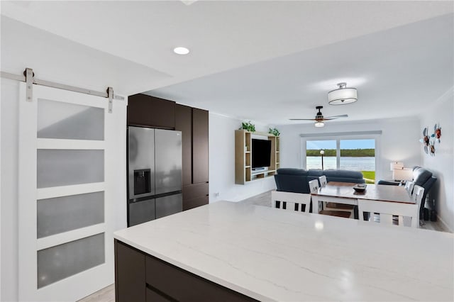 kitchen with stainless steel fridge, dark brown cabinetry, ceiling fan, a barn door, and light hardwood / wood-style flooring