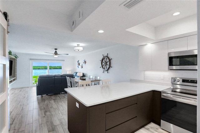 kitchen with light hardwood / wood-style flooring, kitchen peninsula, a water view, white cabinets, and appliances with stainless steel finishes