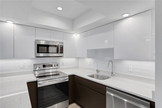 kitchen with sink, tasteful backsplash, light stone counters, white cabinetry, and stainless steel appliances