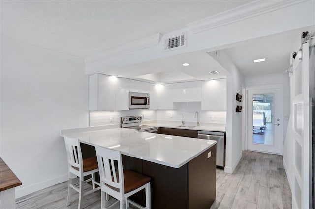 kitchen with white cabinets, sink, appliances with stainless steel finishes, kitchen peninsula, and a breakfast bar area