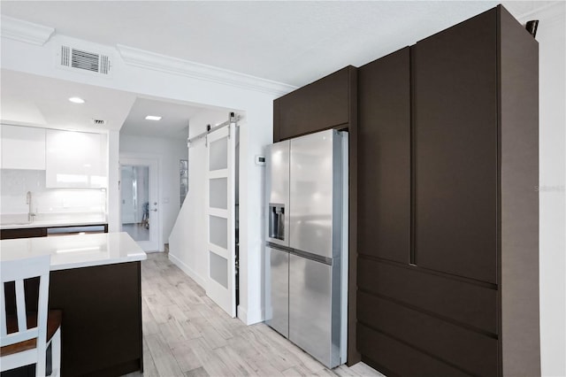 kitchen with white cabinets, a barn door, tasteful backsplash, light hardwood / wood-style floors, and stainless steel fridge with ice dispenser