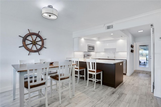 kitchen with kitchen peninsula, appliances with stainless steel finishes, light wood-type flooring, a kitchen bar, and white cabinetry