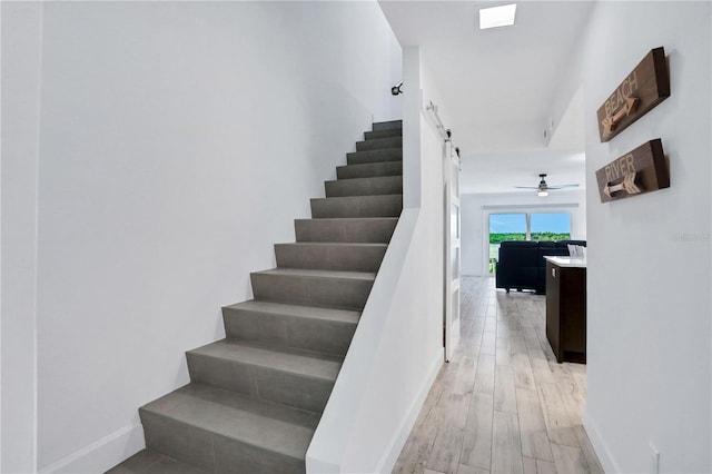 stairway with a barn door, ceiling fan, and hardwood / wood-style floors