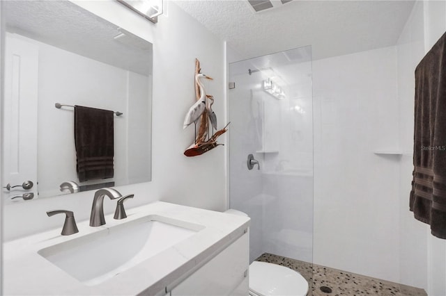 bathroom with tiled shower, toilet, a textured ceiling, and vanity