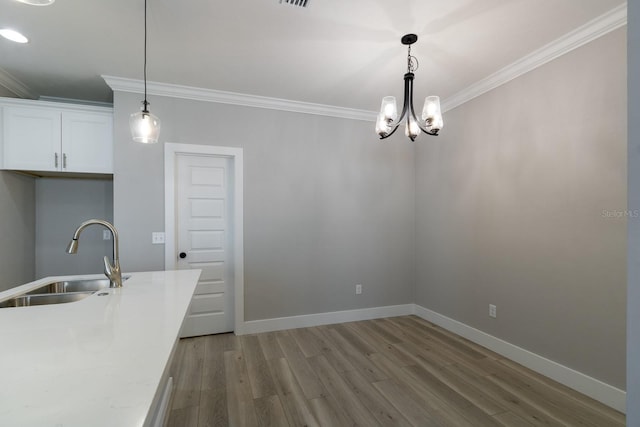 unfurnished dining area with a sink, wood finished floors, an inviting chandelier, crown molding, and baseboards