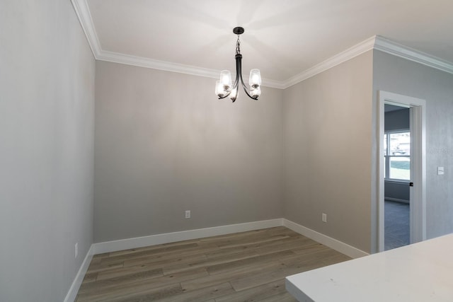 unfurnished dining area featuring an inviting chandelier, wood finished floors, baseboards, and ornamental molding