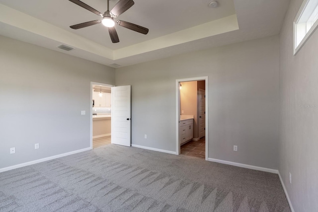 unfurnished bedroom featuring visible vents, baseboards, a tray ceiling, and carpet floors