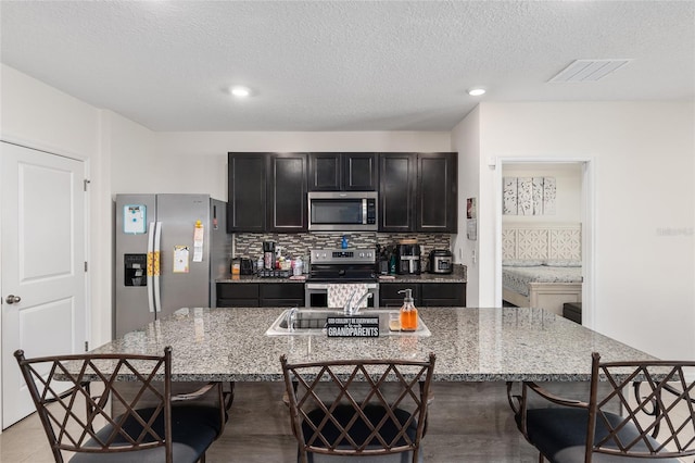 kitchen featuring decorative backsplash, light stone counters, a breakfast bar, a textured ceiling, and stainless steel appliances