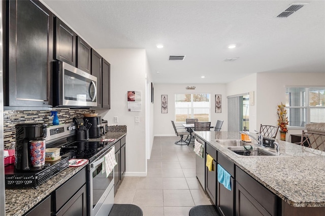 kitchen with sink, backsplash, a kitchen island with sink, light tile patterned flooring, and appliances with stainless steel finishes