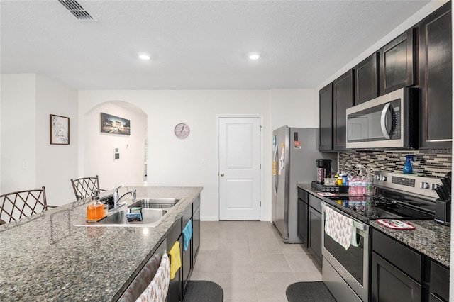 kitchen with dark stone counters, sink, light tile patterned floors, tasteful backsplash, and stainless steel appliances