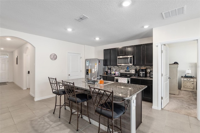 kitchen featuring dark stone countertops, a breakfast bar, light tile patterned flooring, a center island with sink, and appliances with stainless steel finishes