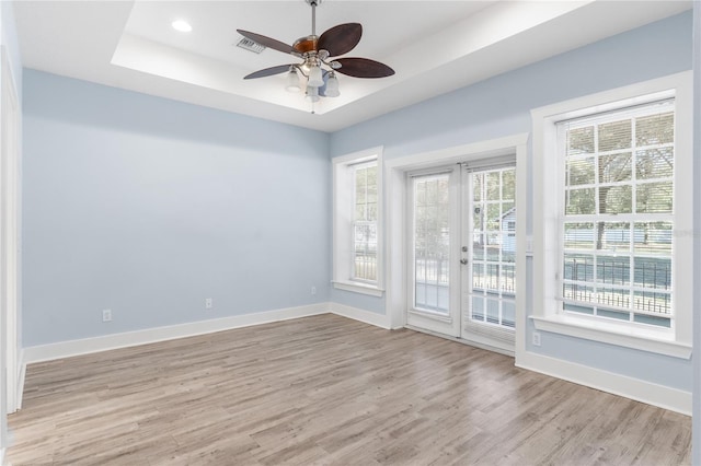 unfurnished room with ceiling fan, light hardwood / wood-style floors, french doors, and a raised ceiling