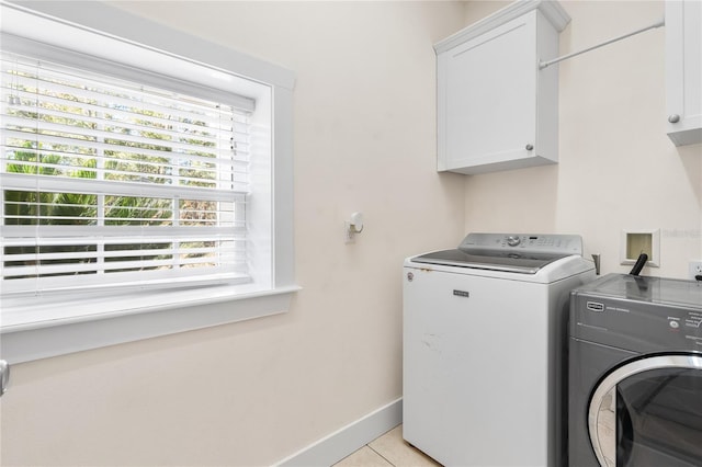 clothes washing area with washer and clothes dryer, light tile patterned floors, and cabinets